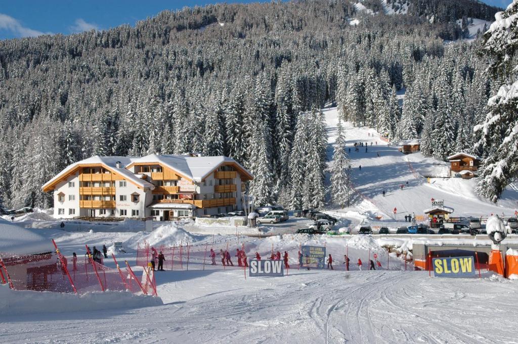 a ski lodge on a snowy mountain with people on a ski slope at Wellness Hotel Lupo Bianco in Canazei