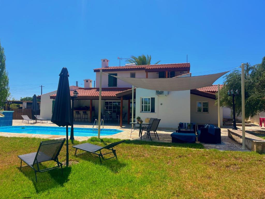 a house with a yard with chairs and an umbrella at Niki villa in Pano Akourdalia