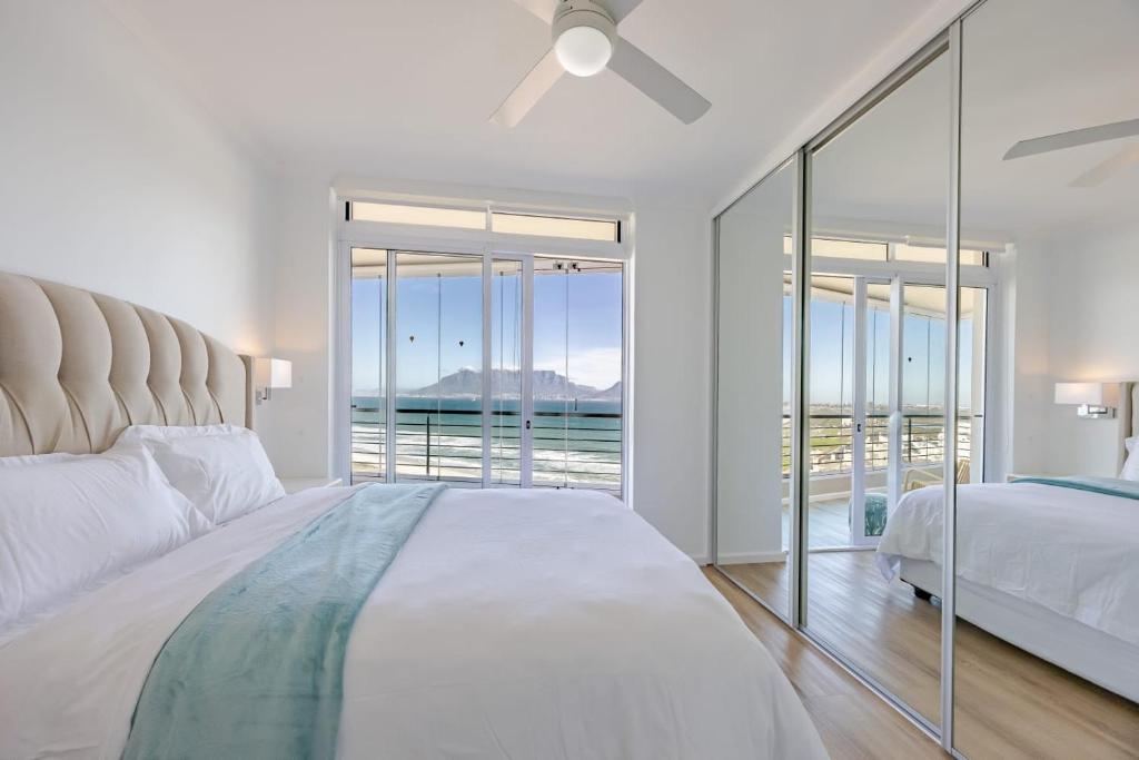 a white bedroom with a bed and a large window at Luxury Beachfront-LaVista with Mountain & Ocean views in Bloubergstrand