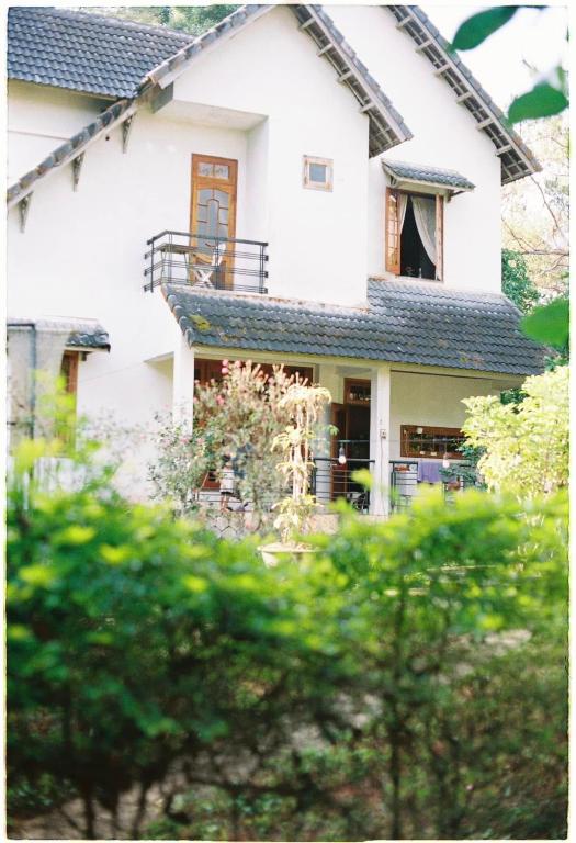 a white house with a balcony and trees at Sum Villa Homestay Mang Den in Kon Von Kla