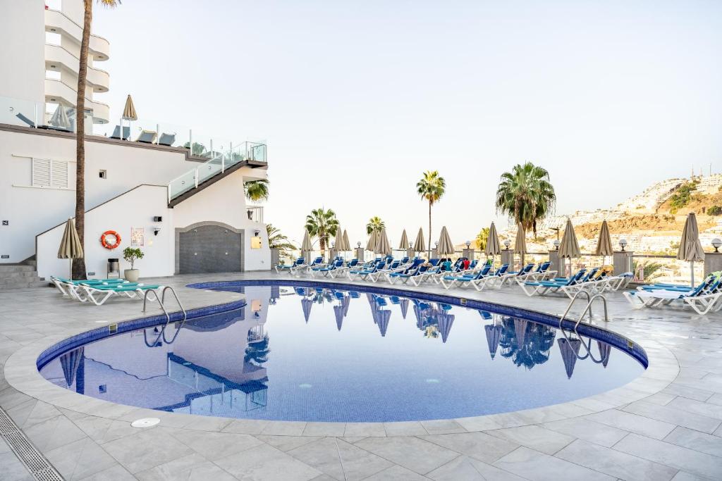 a pool at a resort with chairs and palm trees at Apartamentos Cabau Cala Dor in Puerto Rico de Gran Canaria