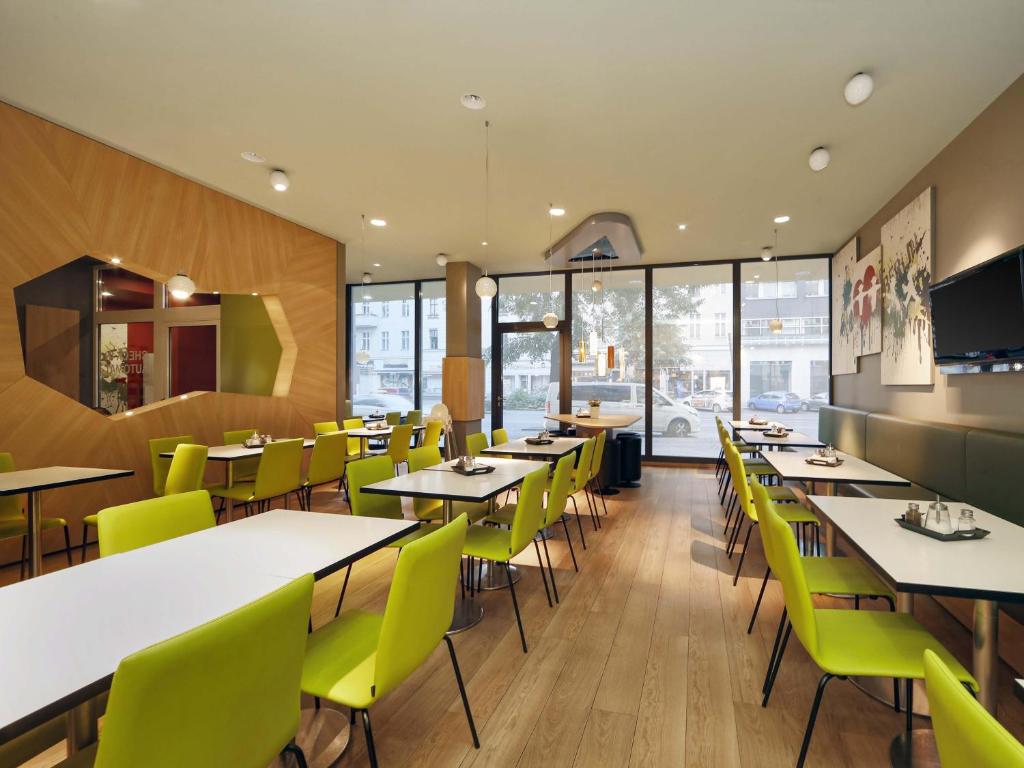 Dining area with green banquettes, white tables, wall-mounted TV, large windows with street view and wood-paneled columns at B&B HOTEL Berlin-Potsdamer Platz in Berlin