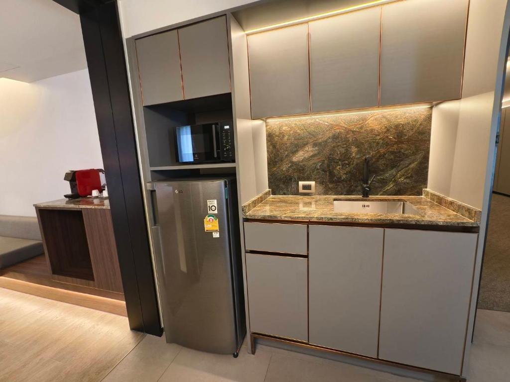 A compact kitchenette with a minibar refrigerator, microwave and illuminated stone backsplash.