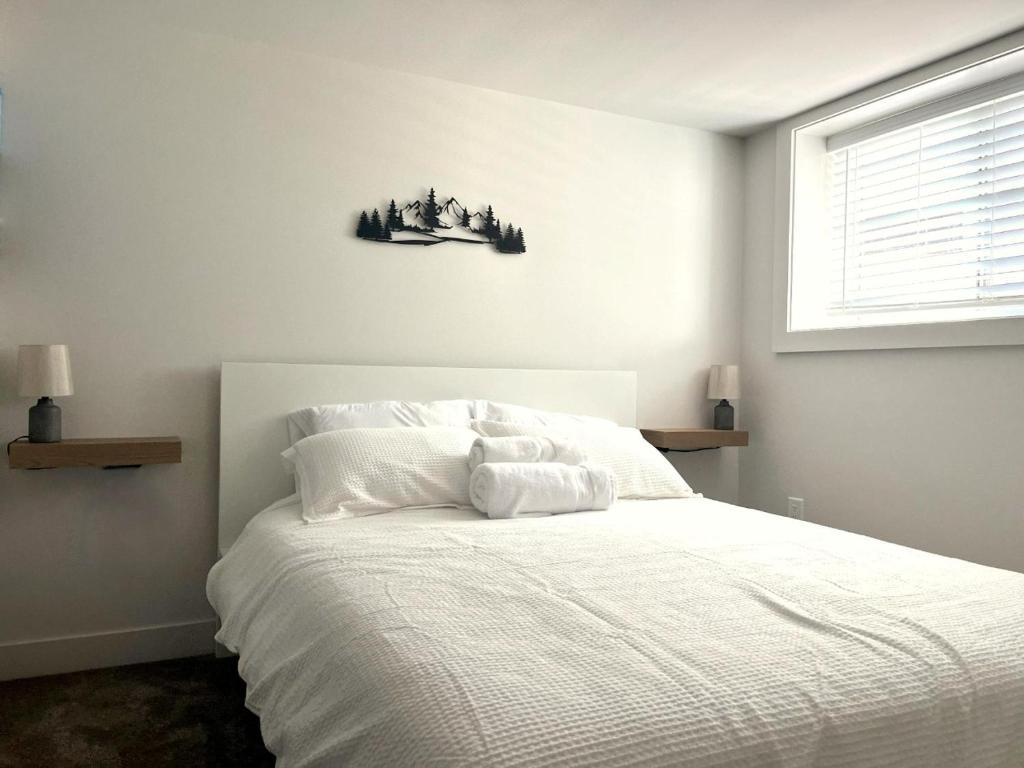 a bedroom with a bed with white sheets and a window at Cedar & Sage Suite - Kitchen & Comfort in Victoria