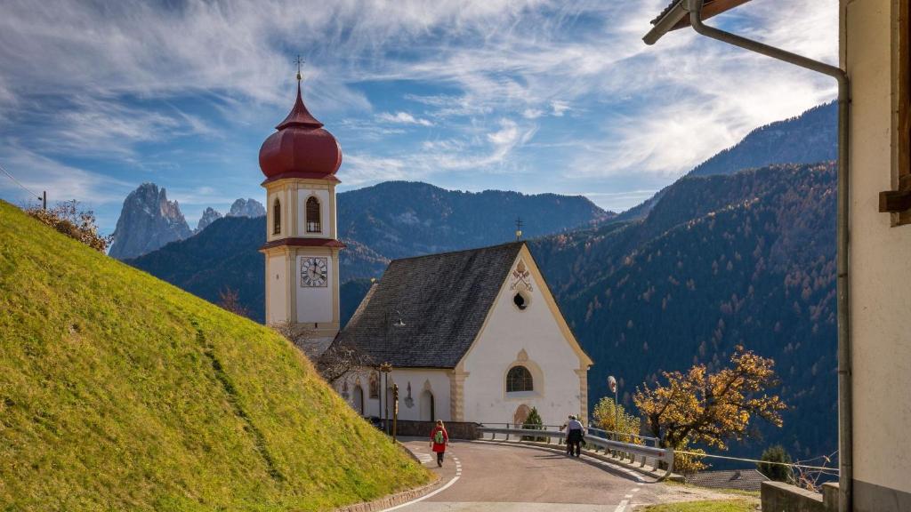 a church with a clock tower on a hill at SAN PIETRO DOLOMITI Small Budget Hotel in Ortisei