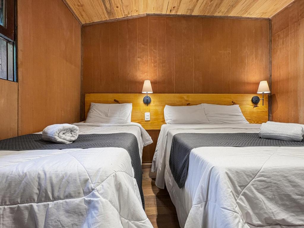 two beds in a room with wooden walls at 1 suíte Jacuzzi Lareira Churrasqueira in Campos do Jordão