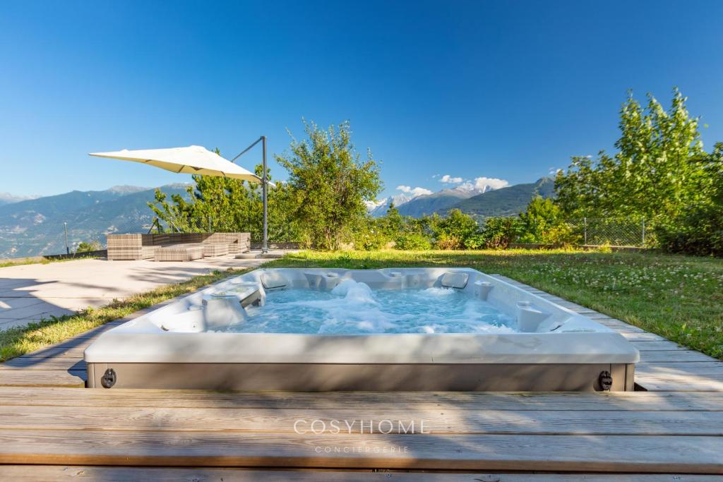 bañera de hidromasaje en una terraza con sombrilla en Le Chalet Pouchignon l Jaccuzzi l By CosyHome, en Savièse