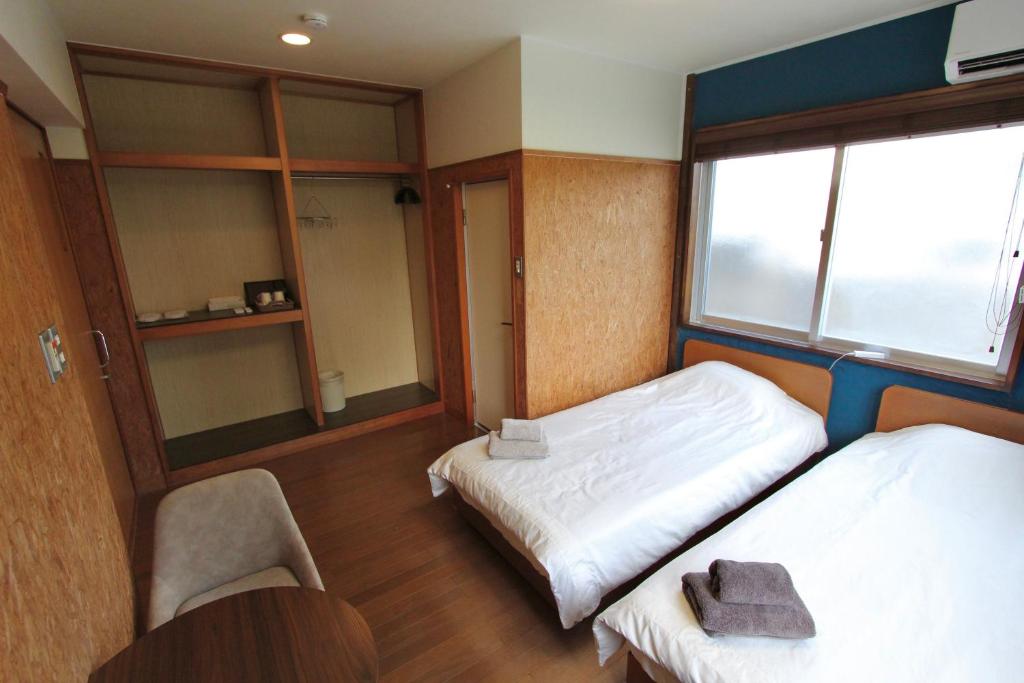 a room with two beds and a chair and a window at 宿 ウラケラマ Urakerama in Aka