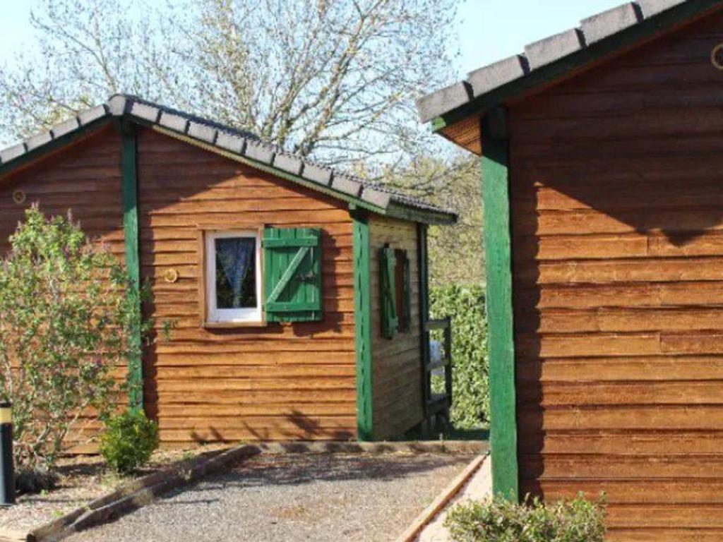 a wooden cabin with a window and a green shutter at Chalet avec Terrasse pour 4 personnes à Naucelle - API-1-52-380 in Naucelle