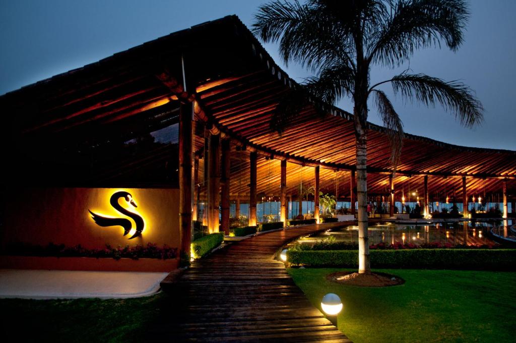 een gebouw met een houten loopbrug naast een palmboom bij El Santuario Resort & Spa in Valle de Bravo