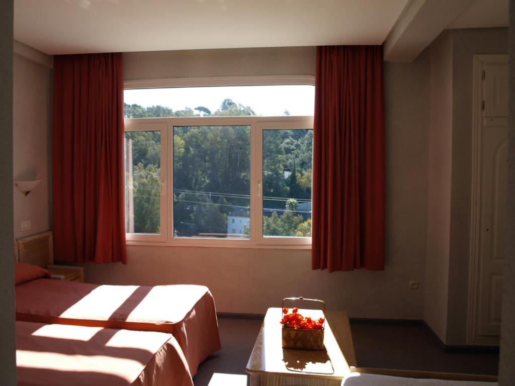1 dormitorio con 2 camas y una ventana con cortinas rojas en Hotel San Jorge, en Alcalá de los Gazules