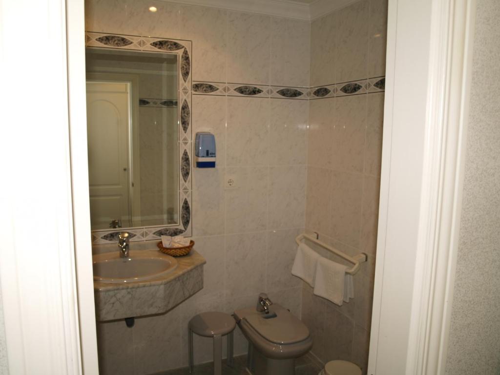 Un baño con lavabo, inodoro y espejo. en Hotel San Jorge, en Alcalá de los Gazules