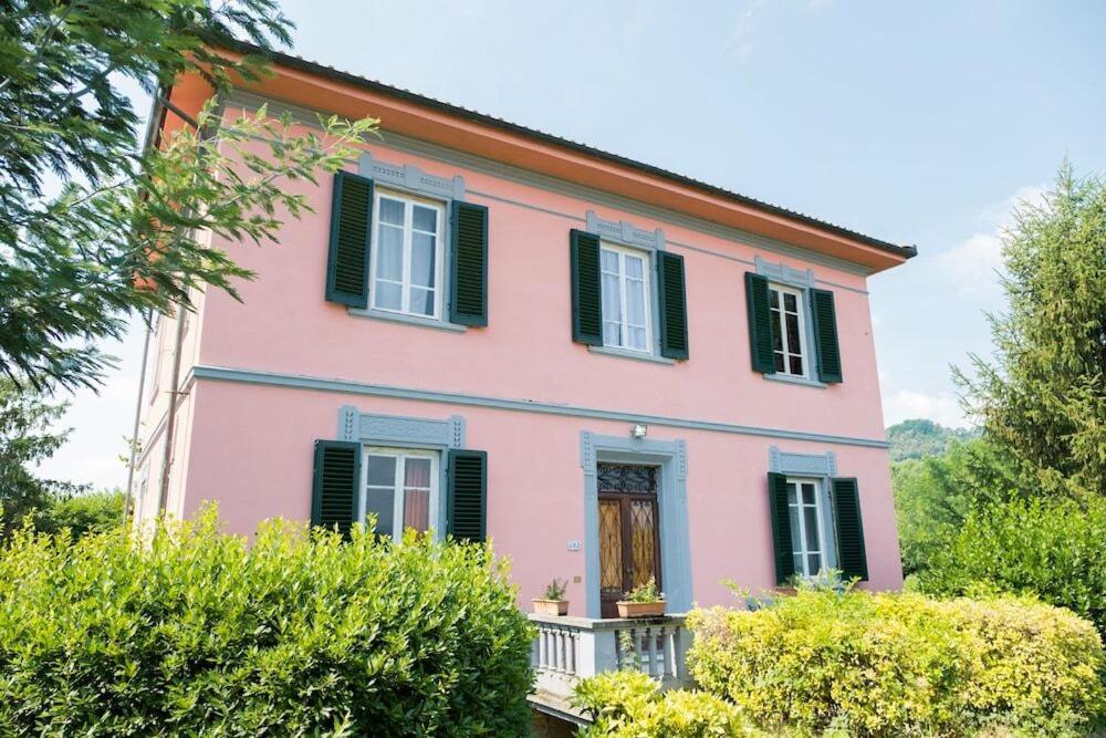 a pink house with green shutters and bushes at Villa Sunrise in Lucca