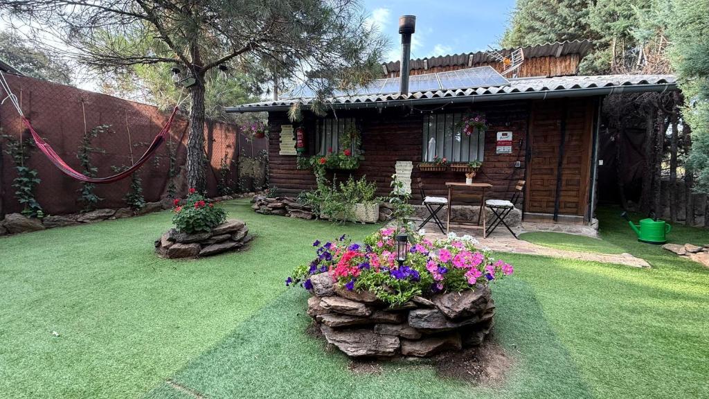 a backyard with a log cabin with flowers in the yard at Cabaña ecologica del lago in Paredes de Buitrago