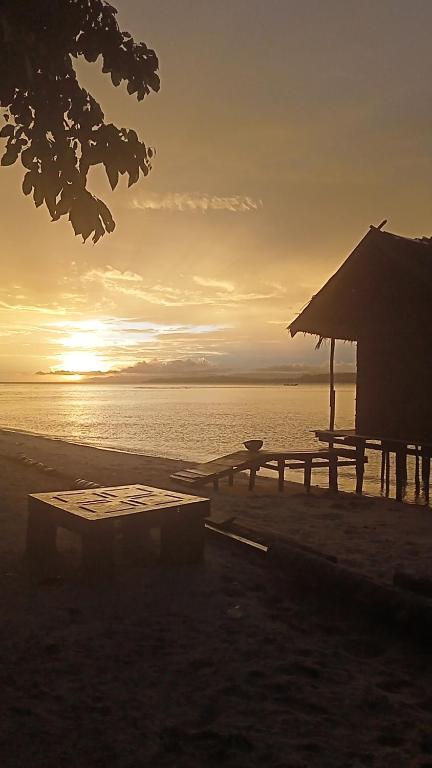 a picnic table and a hut on the beach at sunset at Blacktive Homestay in Kri