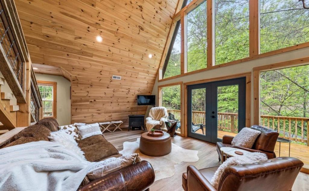 a log cabin living room with leather furniture and large windows at Mountain Haven by Cabin Coco with Swim SPA in Sevierville