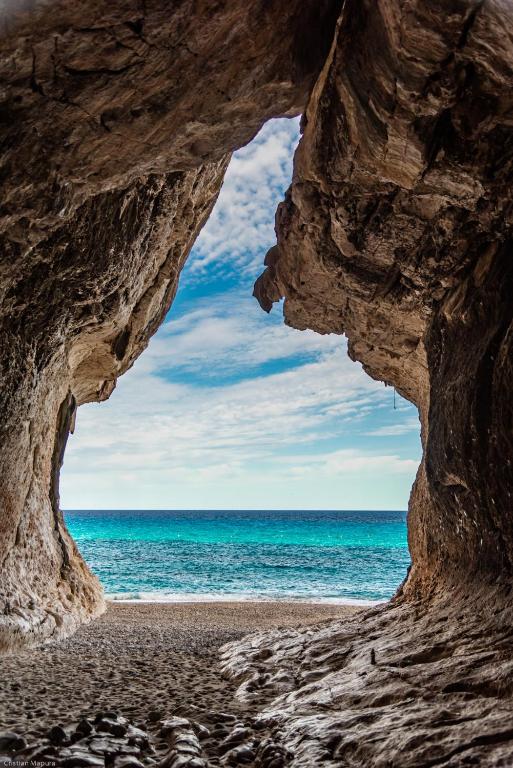 a view of the ocean from a cave on a beach at trilocale con piscina in Arzachena