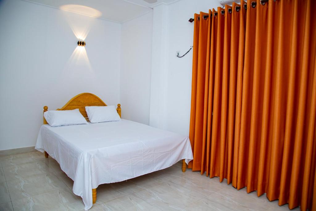 a bedroom with an orange curtain and a bed at Akshaya Villa Trincomalee in Trincomalee