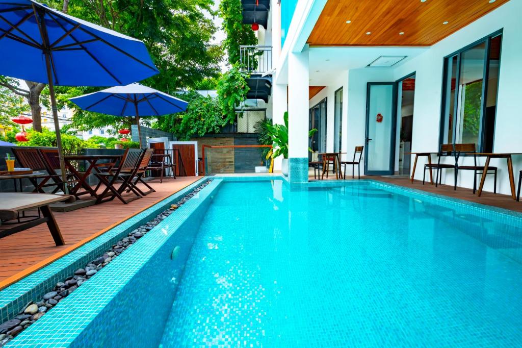 a pool with chairs and umbrellas next to a house at Hoi An Majestic Villa in Hoi An