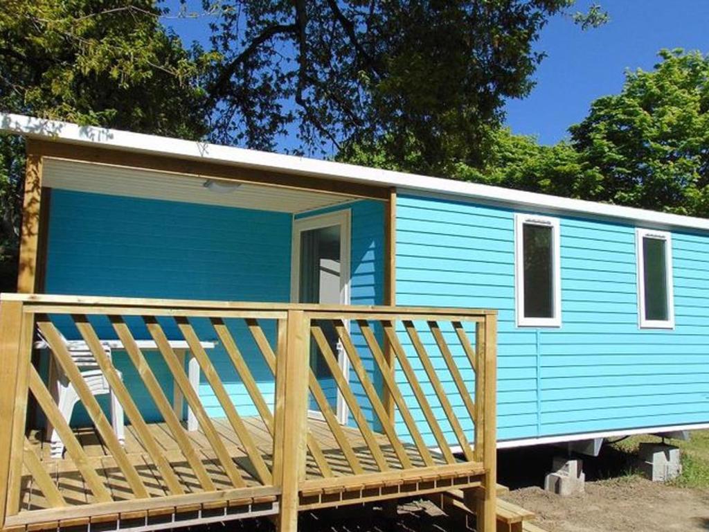 a blue tiny house with a large wooden porch at Mobil-home pour 4 pers avec terrasse - API-1-52-739 in Avrillé