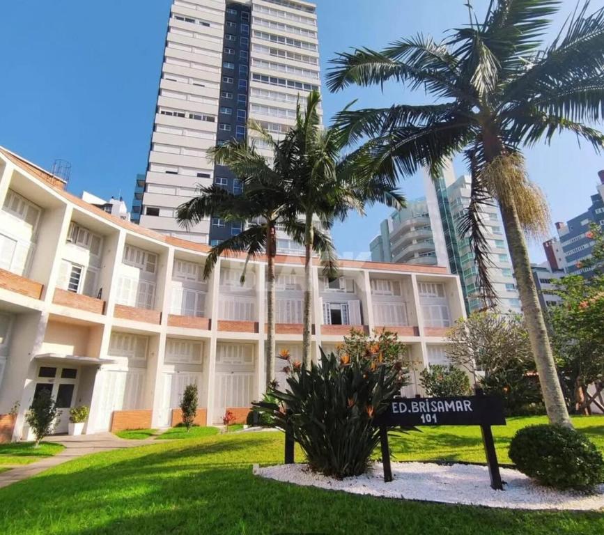a large building with palm trees in front of it at Apartamento Pé na Areia- Torres in Torres