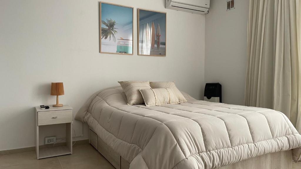 a white bedroom with a bed with a nightstand and a picture at Aire de Mar Alojamiento Necochea in Necochea