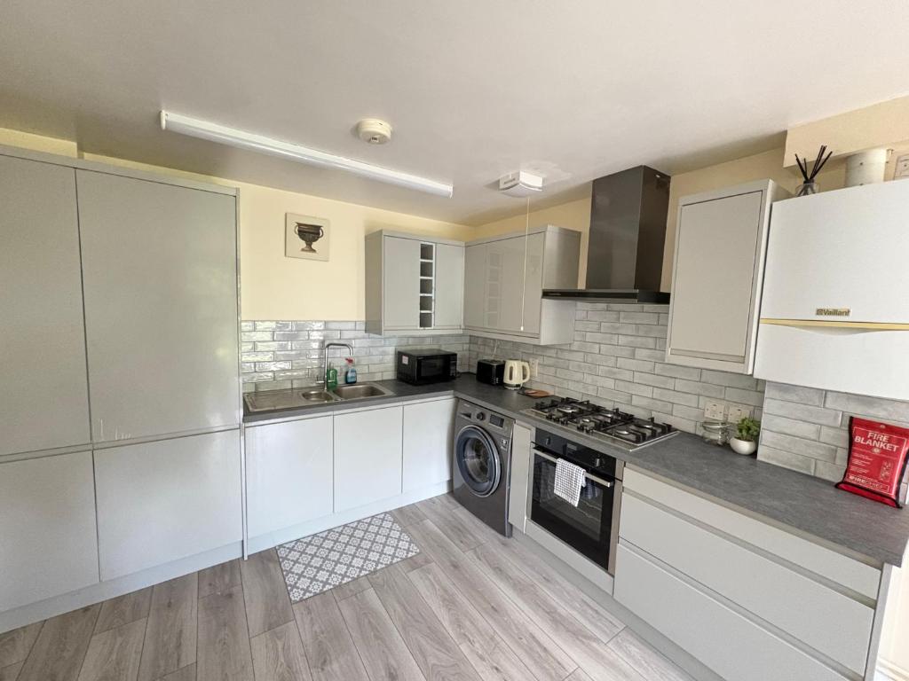 a kitchen with white cabinets and a washer at Cosy 2-Bed Flat Near ExCeL and City Airport in London