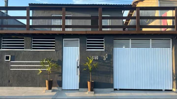 two white garage doors on a building with two plants at Casa Aconchegante de Praia in Caraguatatuba