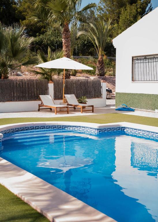 a swimming pool with an umbrella and two lounge chairs at La casa Zamora in Totana
