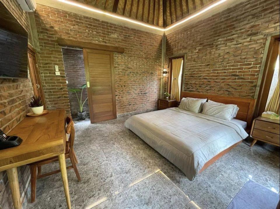 a bedroom with a bed and a desk and a brick wall at Kamanaya Ubud in Ubud