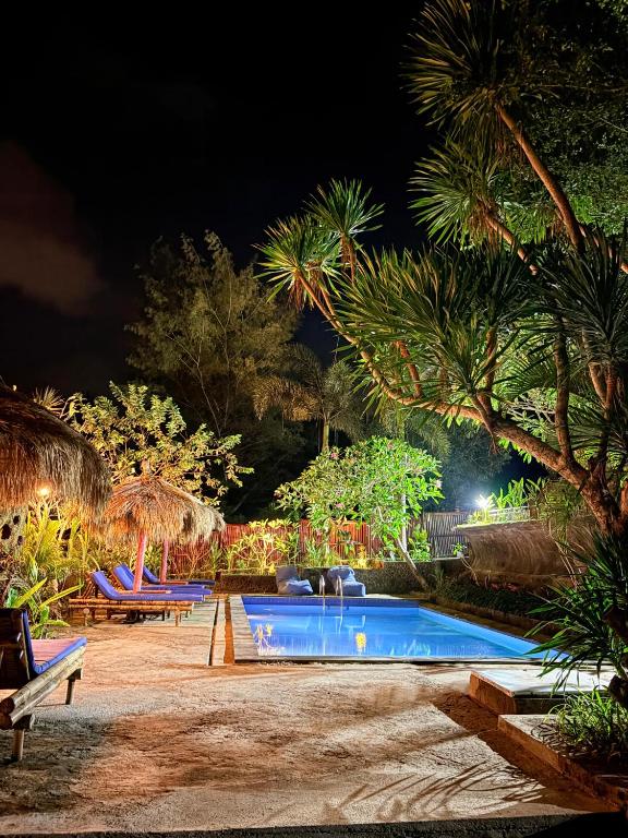 a swimming pool at night with chairs and palm trees at Alfa Kuta in Kuta Lombok