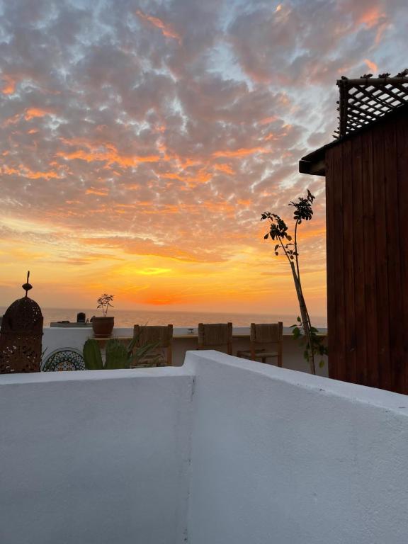a sunset over the beach with a white wall and chairs at Imsouane soul lodge in Imsouane