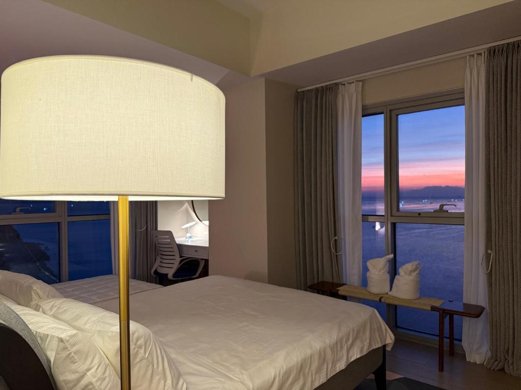 a bedroom with a bed and a lamp and a window at Luxurious 1 Br Facing Manila Bay Sunset Nearby Okada MOA Solaire Ayala Malls in Manila