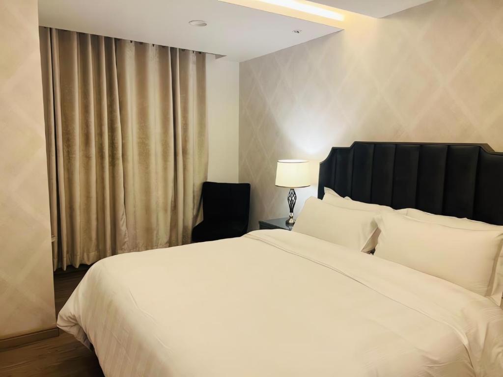 a bedroom with a large white bed and a chair at GoldCrest Mall Luxury Apartments with Balcony In DHA Lahore in Lahore