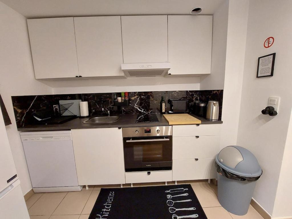 a kitchen with white cabinets and a sink and a trash can at Cosy Home 4 - Spacieux studio avec parking - 30 min Paris in Cergy