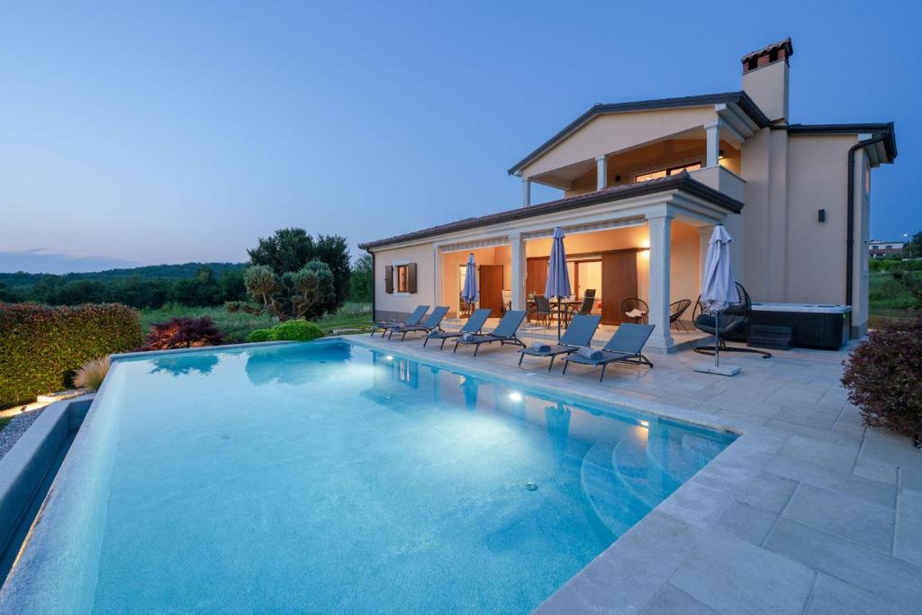 a swimming pool with chairs and a house at Villa Kadore in Višnjan