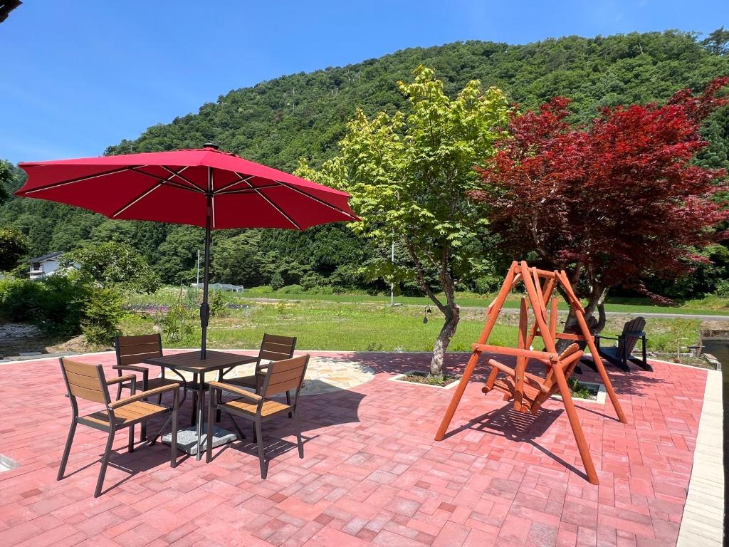 a table and chairs with a red umbrella and a swing at MIYABI Guesthouse in Hakusan
