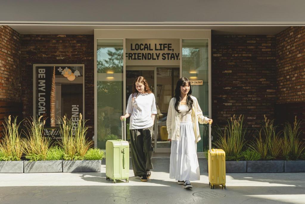 two women walking with luggage in front of a building at Sinchon Local Friends Hotel in Seoul