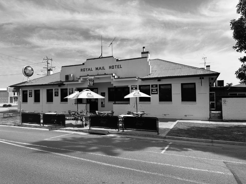 Una foto en blanco y negro de un edificio con mesas y sombrillas. en Royal Mail Hotel Mulwala, en Mulwala