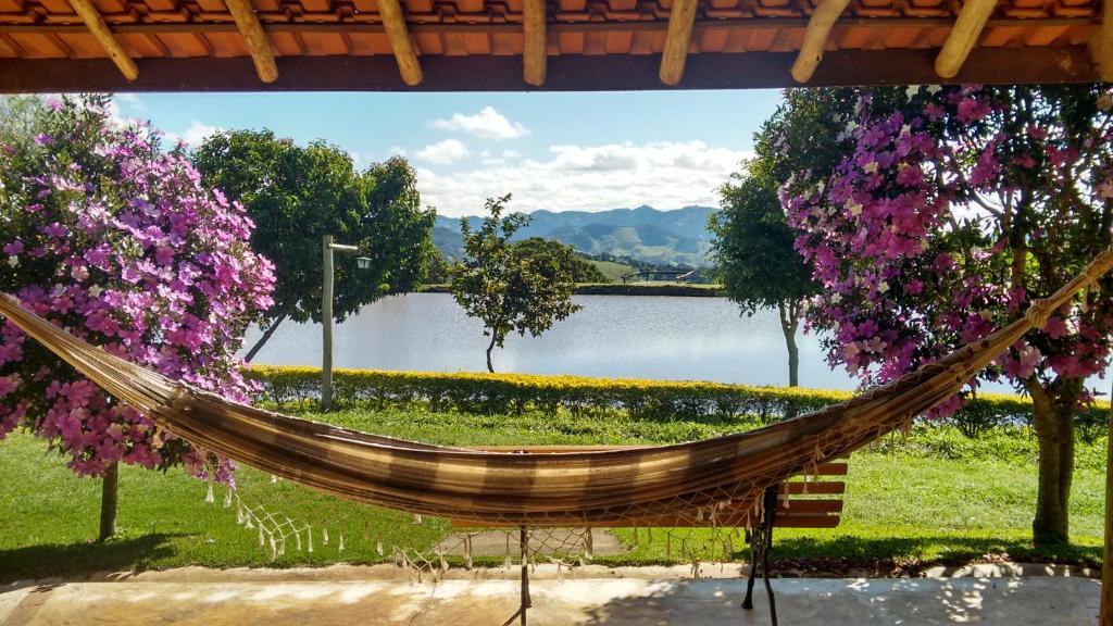 a hammock in front of a lake with flowers at Tocas do Lago in São Bento do Sapucaí