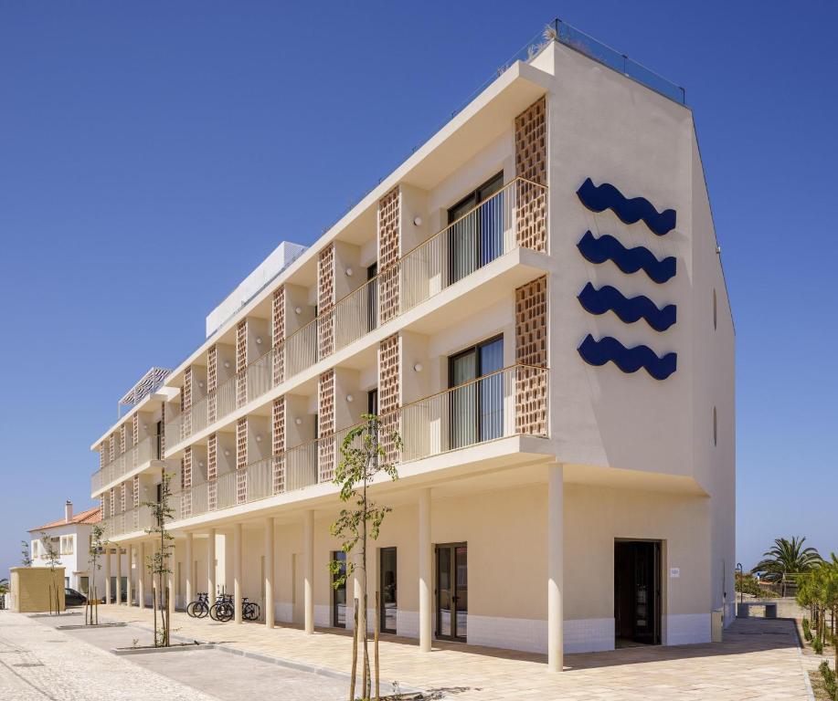 a white building with a blue sign on it at Amarello Hotel Praia Santo André, Tapestry Collection by Hilton in Santiago do Cacém