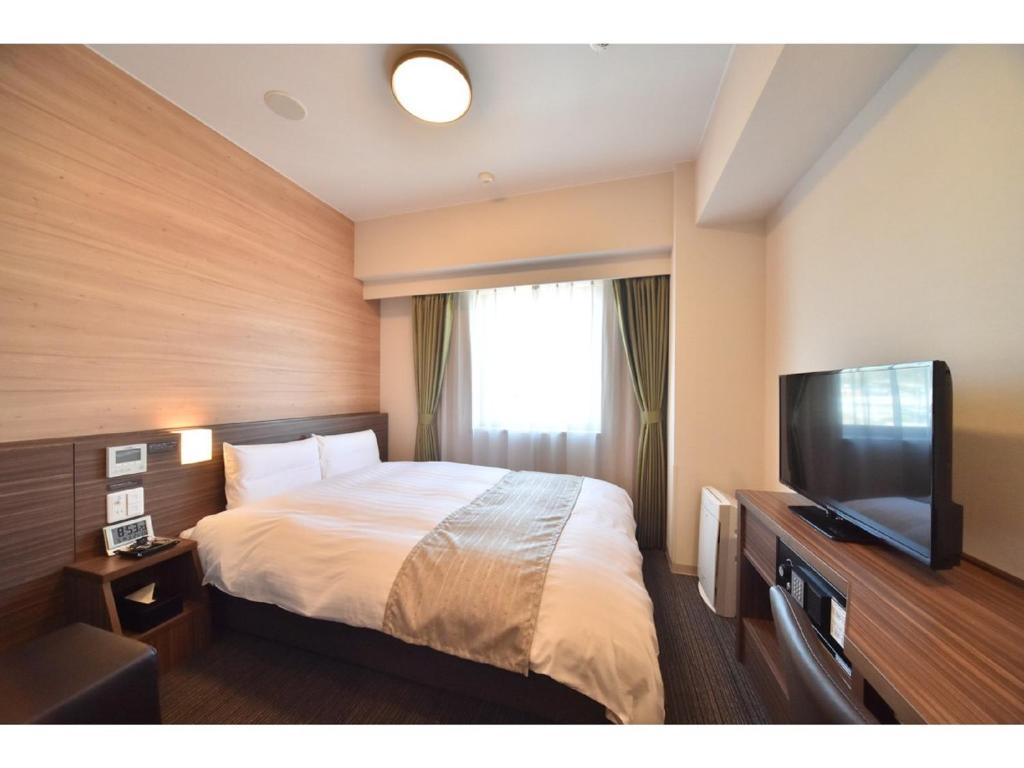 a hotel room with a bed and a flat screen tv at Dormy Inn Abashiri in Abashiri