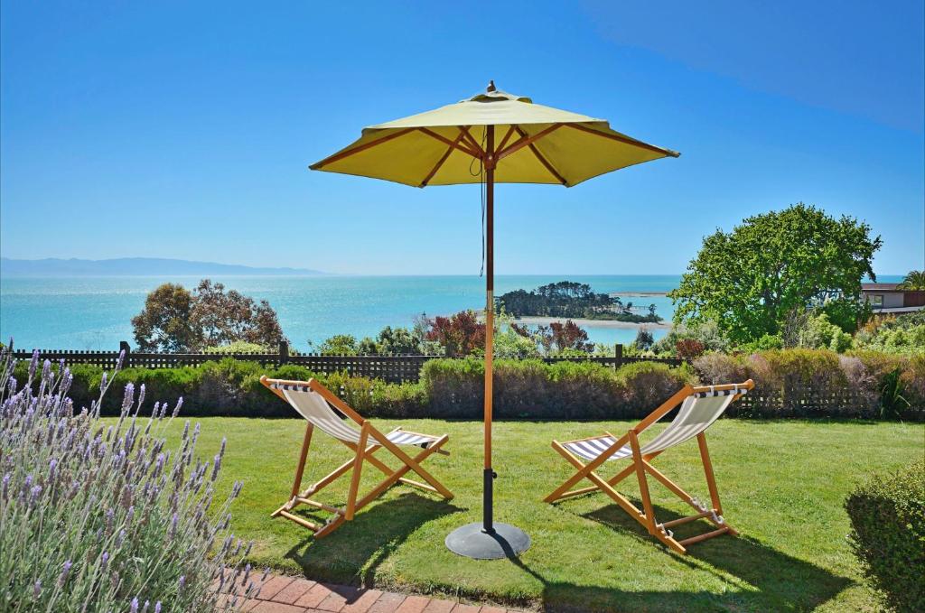 two chairs and an umbrella in the grass at The Cliffs - Nelson Waterfront Home in Nelson