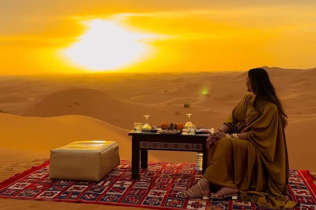a woman sitting in front of a table in the desert at Sahara Family Luxury Camp in Merzouga