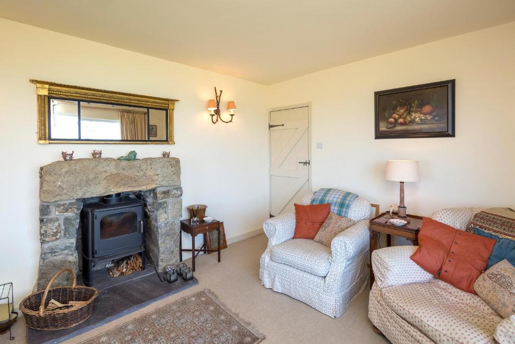 a living room with a stone fireplace and two chairs at Rhiw 2 Bryn Tirion in Rhiw