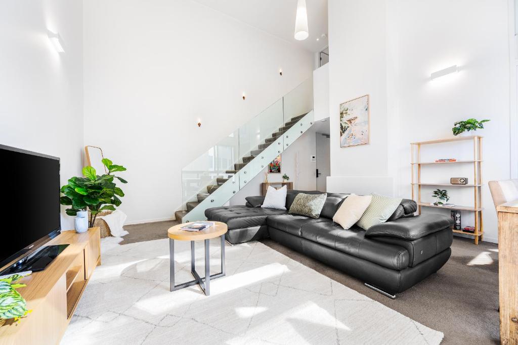 メルボルンにあるFoundry Top Floor 2BR Loft Parking & Workspaceのリビングルーム(黒い革張りのソファ、テレビ付)