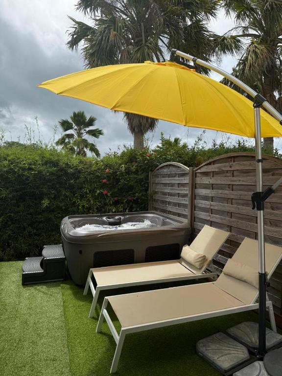 a hot tub with a yellow umbrella and chairs at Ti Kaz Paradise in Le Diamant