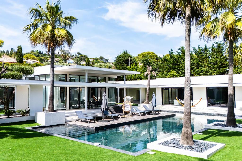 an exterior view of a house with a swimming pool and palm trees at Villa L'oasis, piscine intérieur, extérieur sauna, cinéma in Mougins
