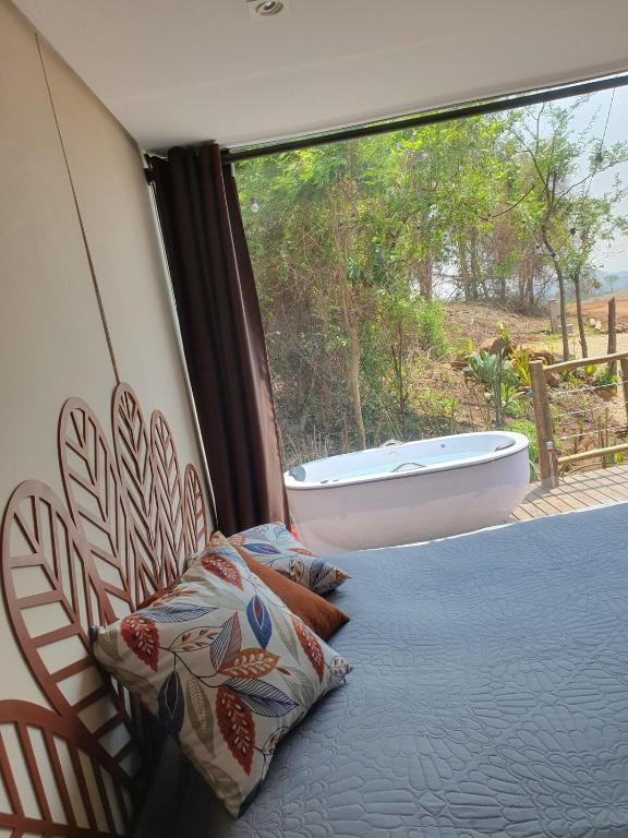 a bedroom with a large window with a bath tub at Container Beija-Flor com SPA e Cachoeira in Brotas
