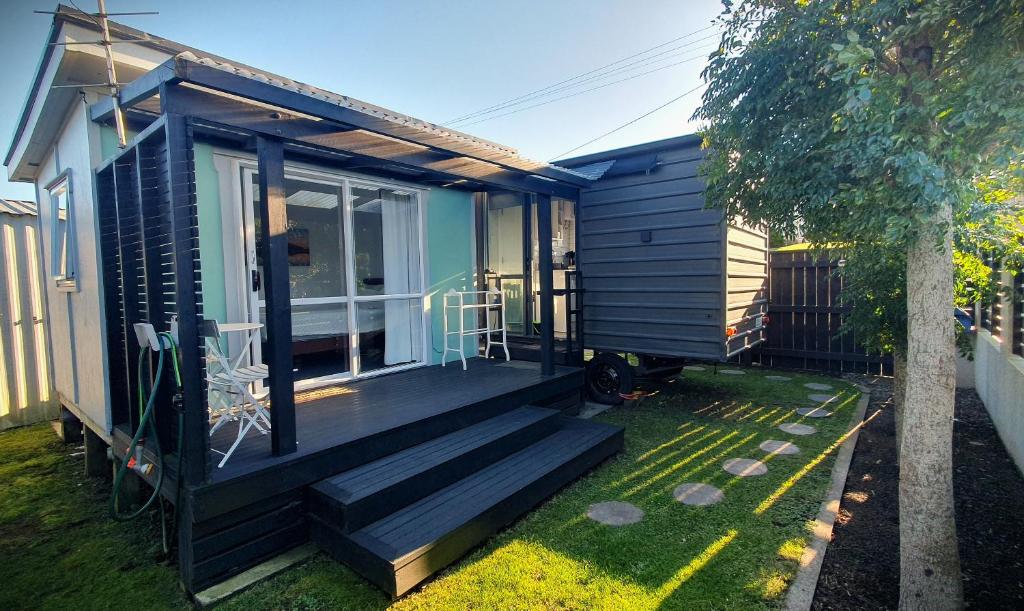 a black tiny house with a porch and a window at Cozy Tiny House in Garden Setting, 3 Minute Drive to Back Beach in New Plymouth